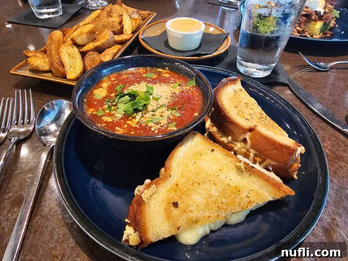 grilled cheese and tomato soup on a blue plate next to potato wedges and aioli sauce