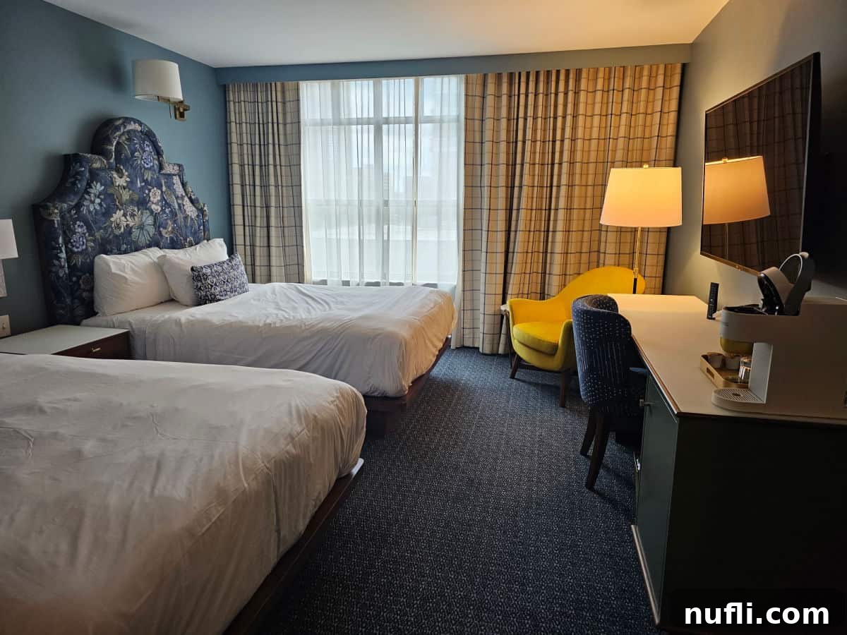 two wueen beds, yellow chair next to a lamp, and work desk in Bradley hotel room