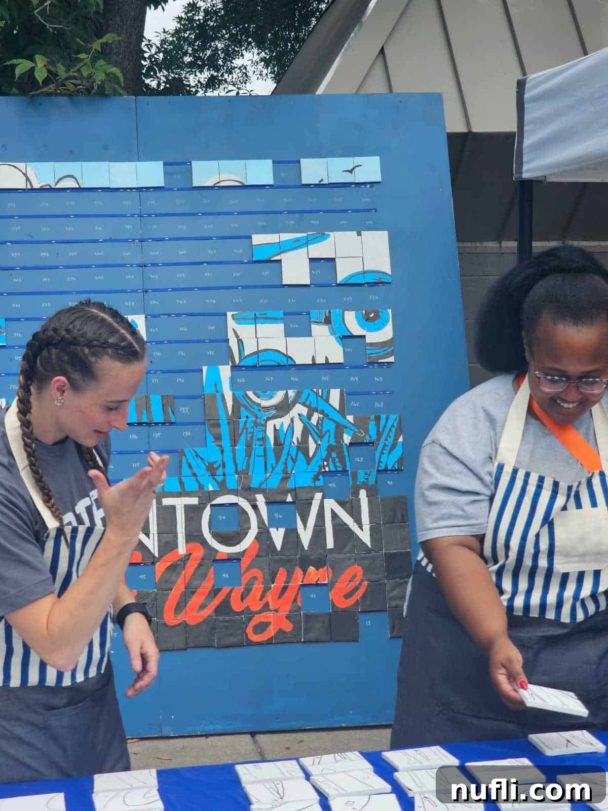 Two people standing with canvas squares next to a large fort wayne art project