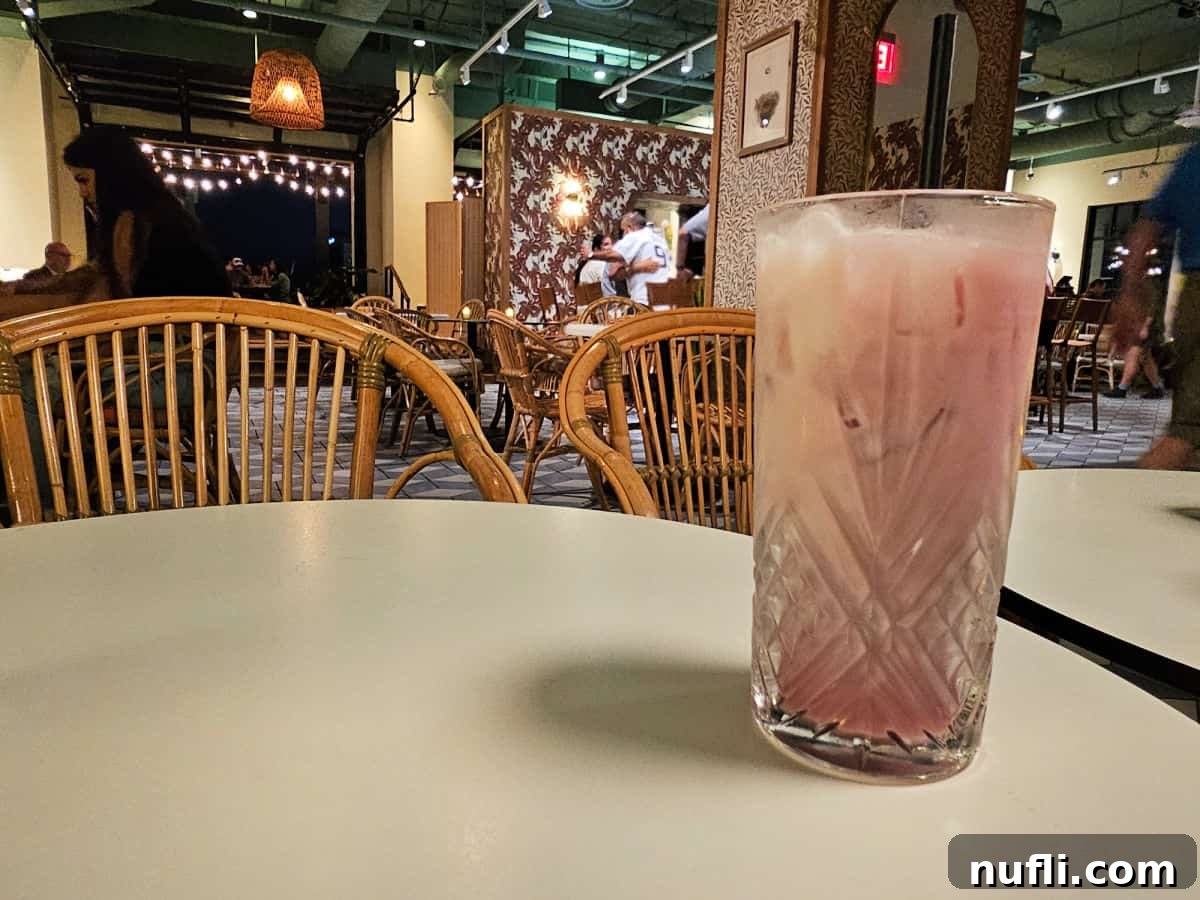 tall glass with pink cocktail on a tabl ewith birdies rooftop bar in the background