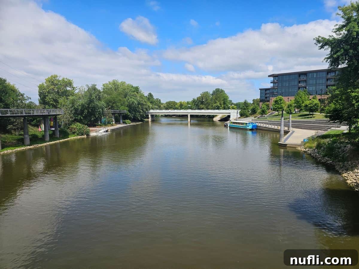 river with a blue boat to one side, hanging kayaks on the other side and walkway over the river