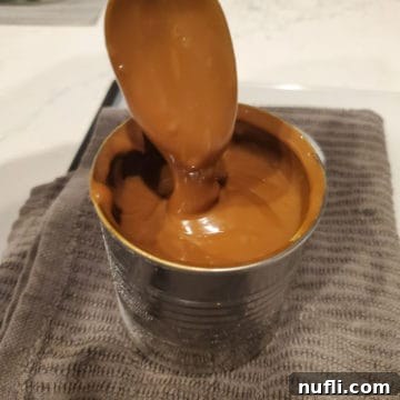 Easy Crockpot Caramel Sauce 4 Spoon covered in caramel sauce coming out of a jar