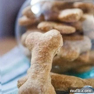 Natural Flea Repellent Dog Biscuits Recipe 4 A single dog biscuit leaning against a clear glass bowl filled with more homemade biscuits, emphasizing the golden-brown color and crunchy texture.