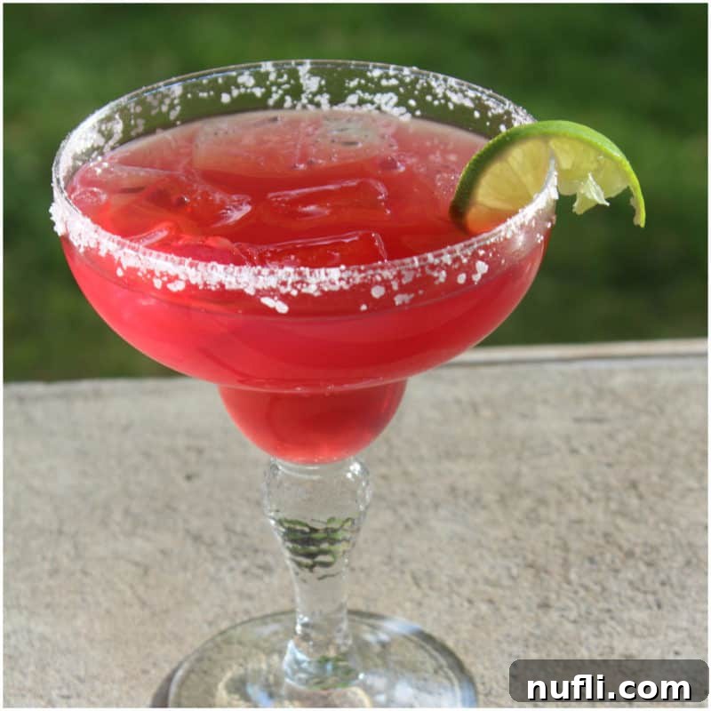 Delicious Tequila Drinks Made Easy 11 A vibrant red margarita in a margarita glass, featuring a salted rim and a fresh lime wedge