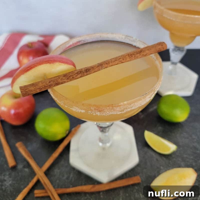 Delicious Tequila Drinks Made Easy 13 An inviting Apple Cider Margarita, garnished with a cinnamon stick, surrounded by fresh apples and lime wedges, signaling autumnal flavors