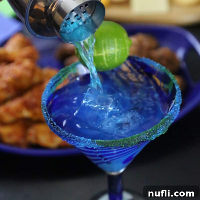 Delicious Tequila Drinks Made Easy 9 A cocktail shaker pouring a vibrant blue Hawk-a-Rita into a margarita glass, garnished with a lime cut into a football shape