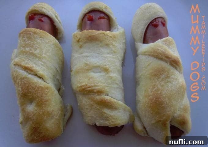 Three perfectly wrapped crescent hot dogs, artfully arranged to resemble mummies, with 'Mummy Dogs' text alongside, inviting you to create these festive treats.