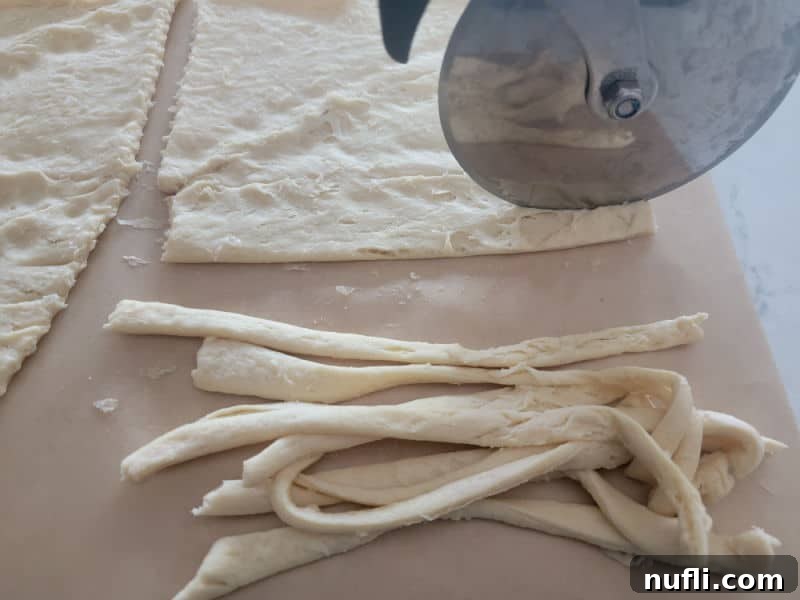 A pizza cutter efficiently slicing crescent roll dough into thin strips, preparing them for wrapping around hot dogs to create mummy bandages.