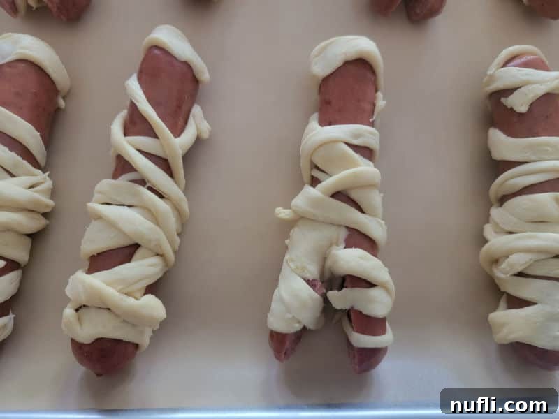 Hot dogs expertly wrapped in crescent roll strips, resembling mummies, ready to be baked into a delicious Halloween treat.