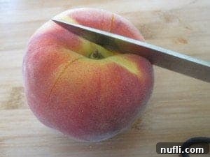A sharp knife making shallow cuts into the skin of a peach, preparing it for easy peeling.