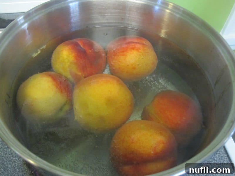 Several peaches submerged in a large pot of boiling water during the blanching process.