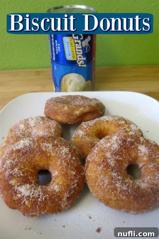 Freshly made Biscuit Donuts piled on a plate, with a can of Grands biscuits in the background, signifying their origin.