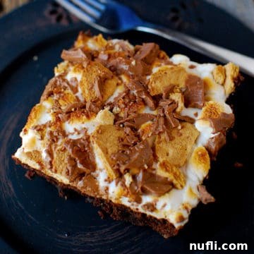 Ultimate S'mores Brownies 3 A perfectly toasted S'mores Brownie Square on a dark plate next to a fork, ready to be enjoyed.