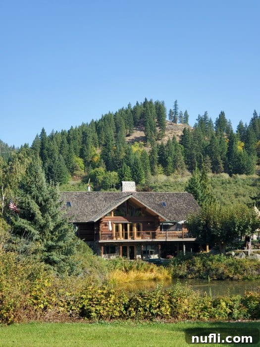 The grand log home of Icicle Ridge Winery, surrounded by lush trees and overlooking a tranquil pond and vineyard.