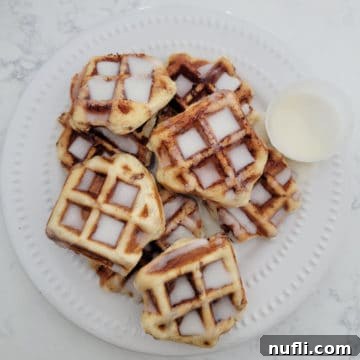 Stack of Cinnamon Roll waffles covered in icing on a white plate