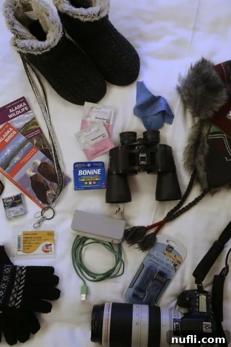 Your Complete Guide to Alaska Cruise Packing 4 boots, binoculars, hat, camera, glovers, charger, bonine, alaska bird guide on a bed