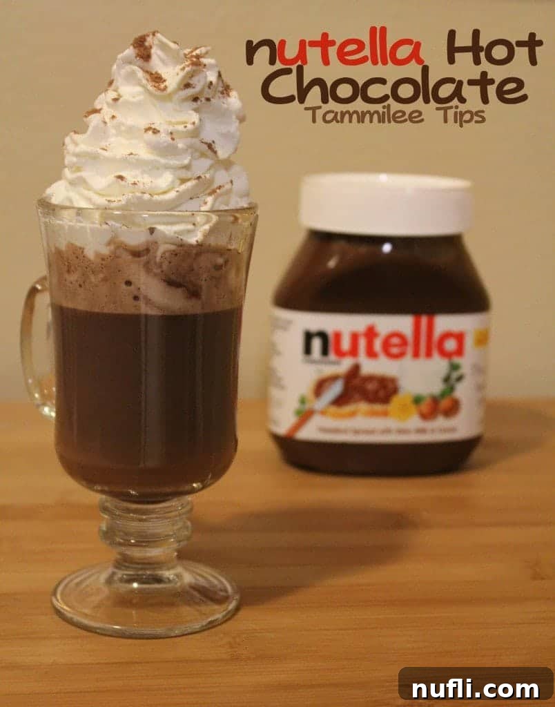 A steaming glass coffee mug filled with creamy Nutella Hot Chocolate, generously garnished with fluffy whipped cream and a sprinkle of chocolate shavings. A jar of Nutella sits nearby, hinting at the key ingredient.