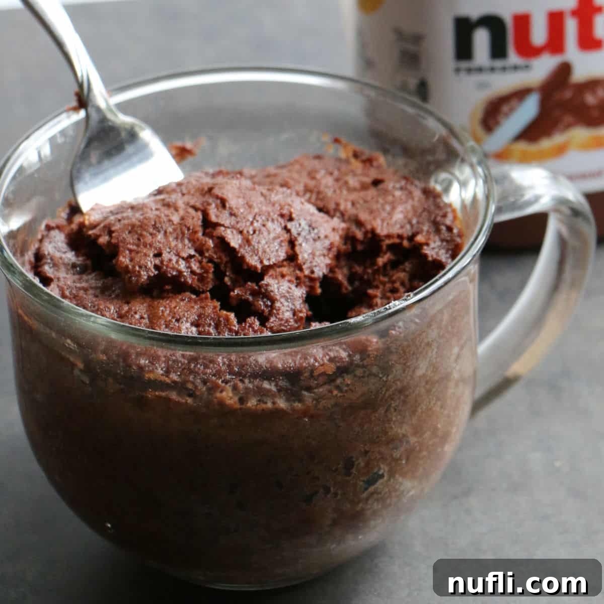 A warm, gooey Nutella Mug Cake served in a clear glass mug, with a fork poised to dig in.