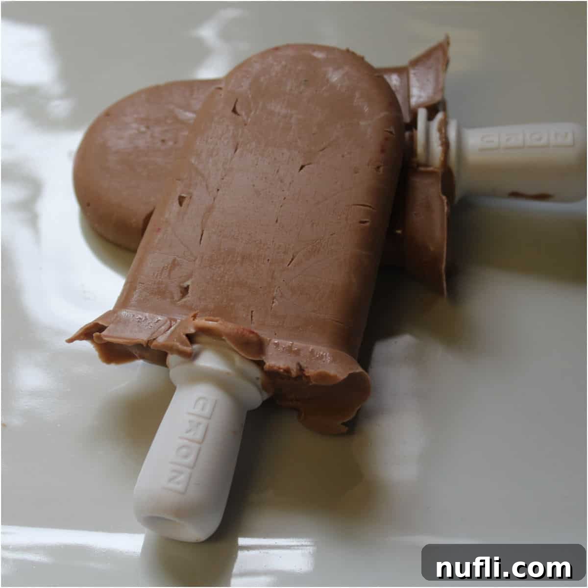 Two enticing Nutella Popsicles resting on a clean white platter, hinting at a cool, chocolatey treat.