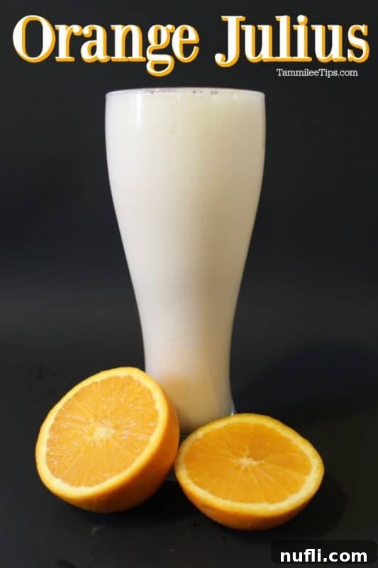Orange Julius in a tall glass with fresh oranges at the base