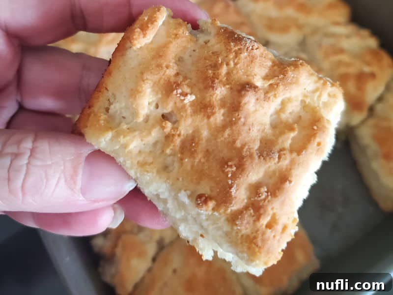 A perfectly baked 7 Up biscuit held in a hand, above a pan full of more biscuits