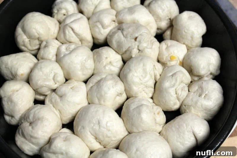 Neatly arranged biscuit dough balls, stuffed with cheddar cheese, forming a tight circle within a round baking dish, ready for their Parmesan topping.