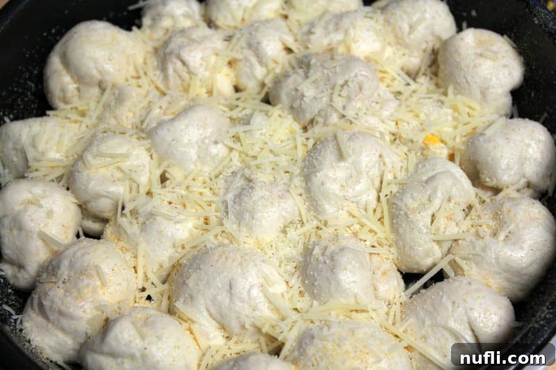 The baking dish now holds the biscuit dough balls, generously covered with a layer of shredded Parmesan cheese, ready for baking.