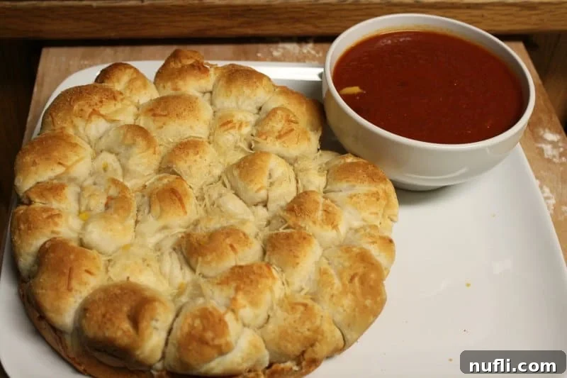 A elegant white platter showcasing warm, golden-brown cheesy biscuit balls arranged around a small, inviting bowl of marinara sauce, ready to be enjoyed.