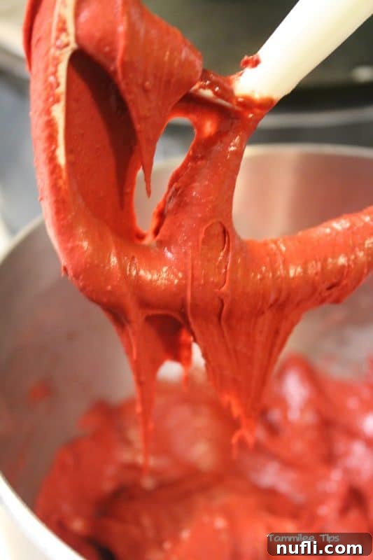 Thick red velvet brownie batter dripping from a mixer attachment, illustrating its consistency.