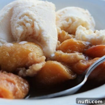 peach crumble topped with vanilla ice cream in a white bowl