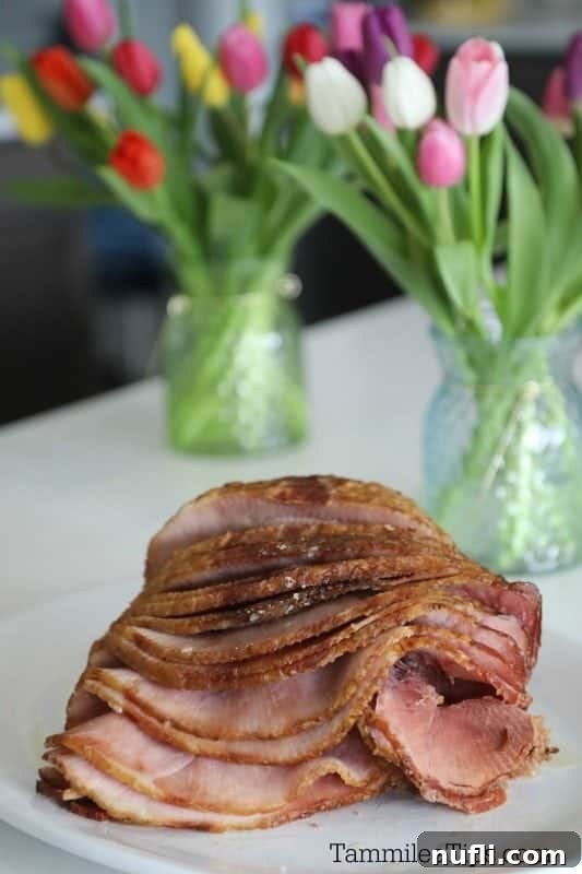Spiral Ham on a white platter with vases of tulips in the background