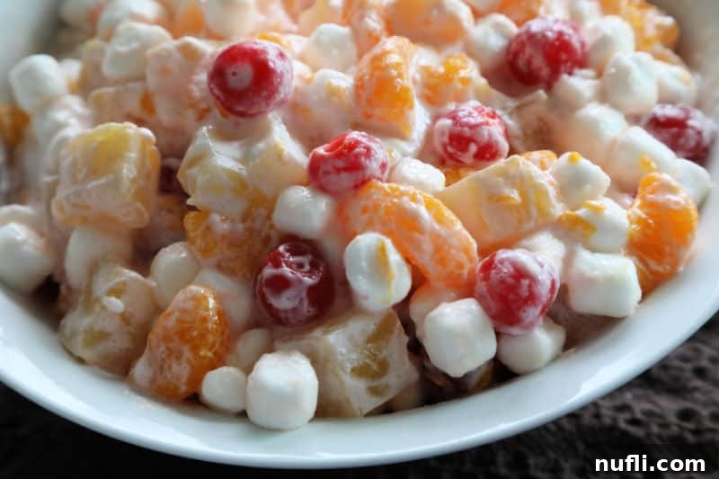 Delicious marshmallow fruit salad presented in a pristine white bowl against a dark background, ready to be served.