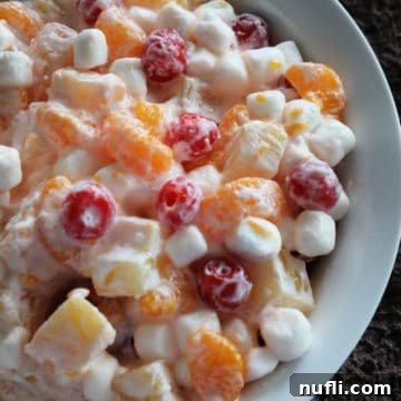Fruit salad with mandarins, pineapples, mini marshmallows, and cherries in a white bowl, ready to be served.