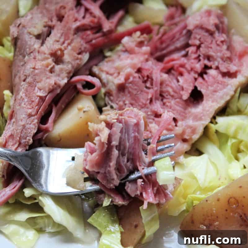 Crockpot Corned Beef and Cabbage on a white plate with potatoes, piece of corned beef on a fork
