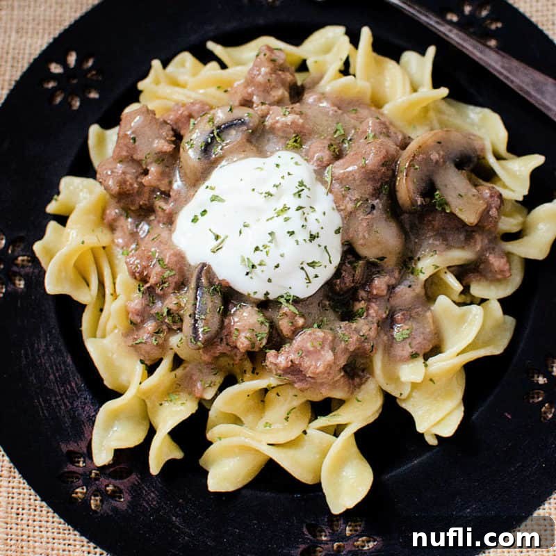 Beef stroganoff garnished with sour cream on a dark plate