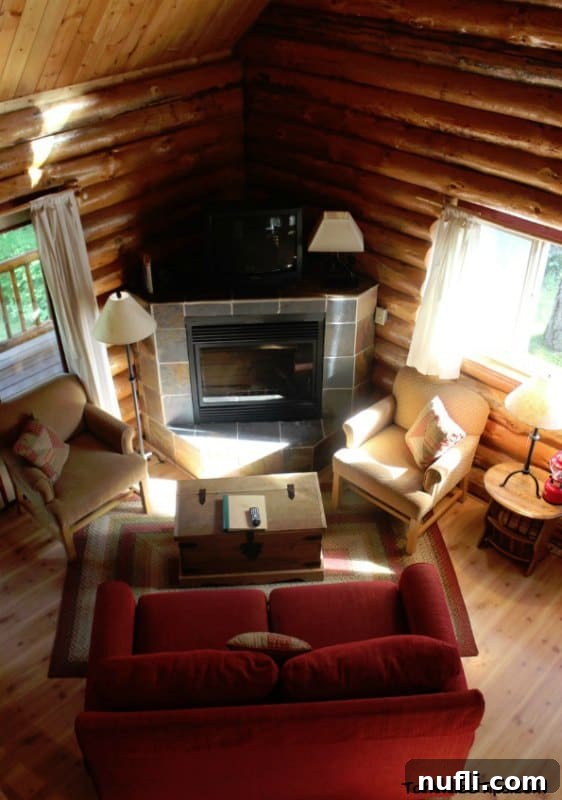 Your Log Cabin Adventure Awaits at Lakedale Resort, San Juan Islands 6 Log cabin interior showcasing a warm fireplace, a vibrant red couch, and comfortable armchairs, creating a cozy and inviting atmosphere.