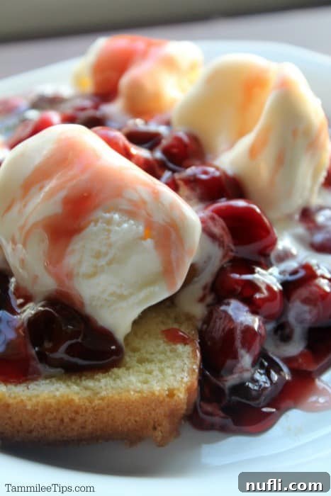 White plate with cherries jubilee on a slice of cake with vanilla ice cream. 