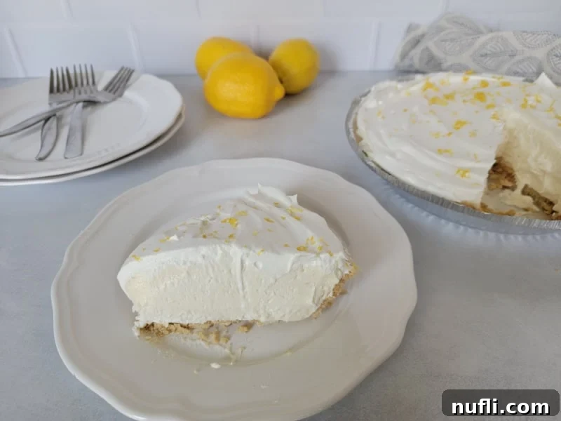 Sunshine Lemon Icebox Pie 9 Slice of no bake lemon pie on a white plate with the full pie in the background.