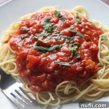 homemade tomato sauce on spaghetti noodles on a white plate next to a fork