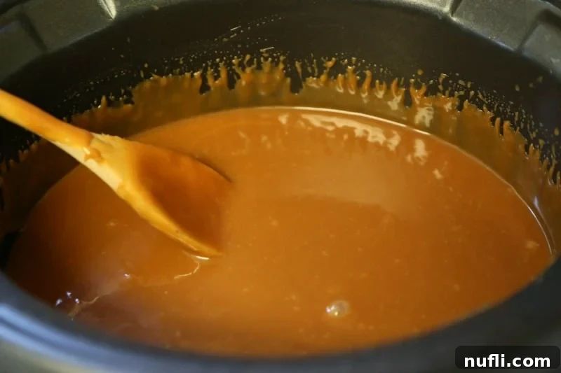 Wooden spoon stirring melted caramel inside a slow cooker, highlighting the smooth texture for dipping