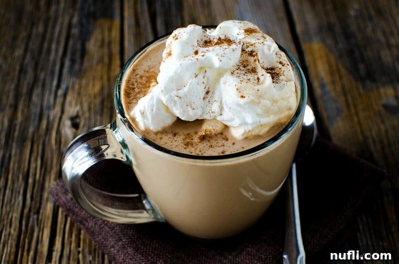 Spiced Slow Cooker Mexican Hot Chocolate 4 A festive glass mug of Mexican hot chocolate topped with whipped cream and cinnamon, placed on a rustic surface, evoking holiday cheer.