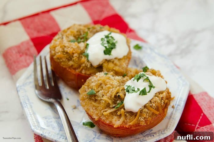 A white plate with a silver fork, featuring a cheese-stuffed tomato topped with sour cream and fresh herbs (basil/parsley).