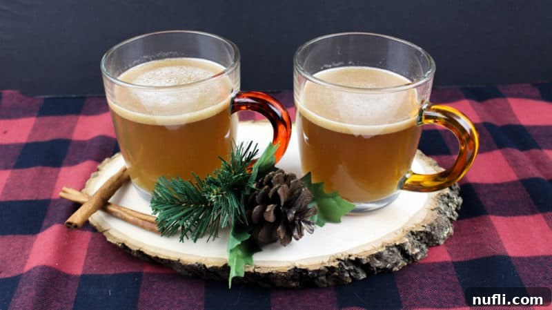 Two mugs of hot buttered rum on a wooden board with cinnamon sticks and a checkered tablecloth