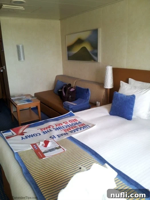 Carnival Breeze stateroom interior featuring a comfortable bed, a charming towel animal, a cozy couch, and a practical table
