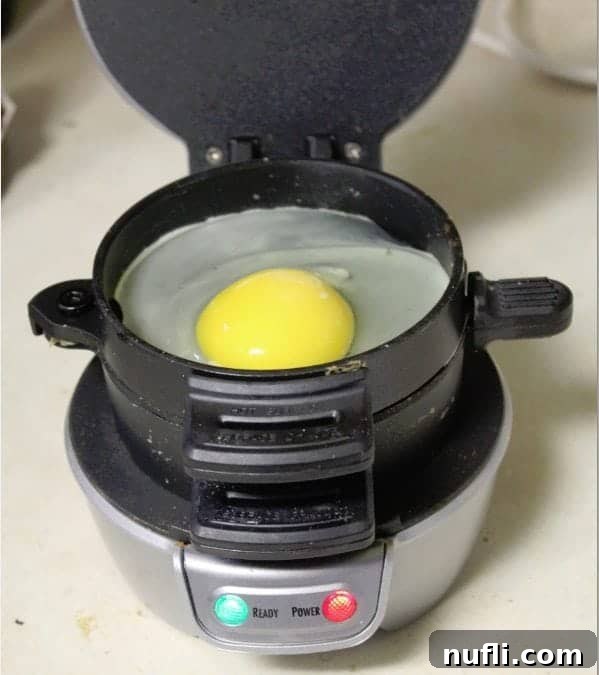 The Ultimate Homemade Breakfast Muffin 4 A fresh egg cracking onto the top layer of a Hamilton Beach Sandwich Maker, ready to cook