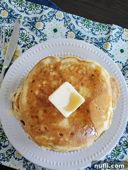 A stack of perfectly cooked Cracker Barrel pancakes on a white plate, topped with a square of melting butter and a drizzle of syrup.