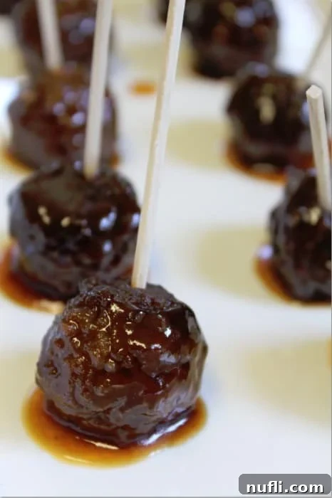 Easy & Delicious 3-Ingredient Grape Jelly Meatballs 4 A white platter filled with grape jelly meatballs, ready to be served as an appetizer with toothpicks.