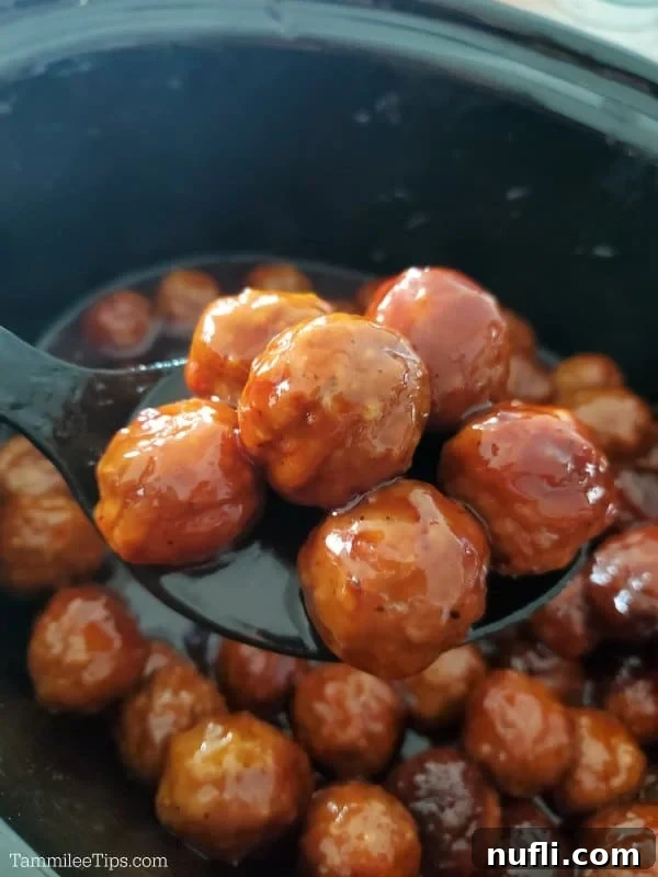 Easy & Delicious 3-Ingredient Grape Jelly Meatballs 5 Grape jelly meatball being served from a black Crock-Pot with a spoon, showing the thick, glossy glaze.
