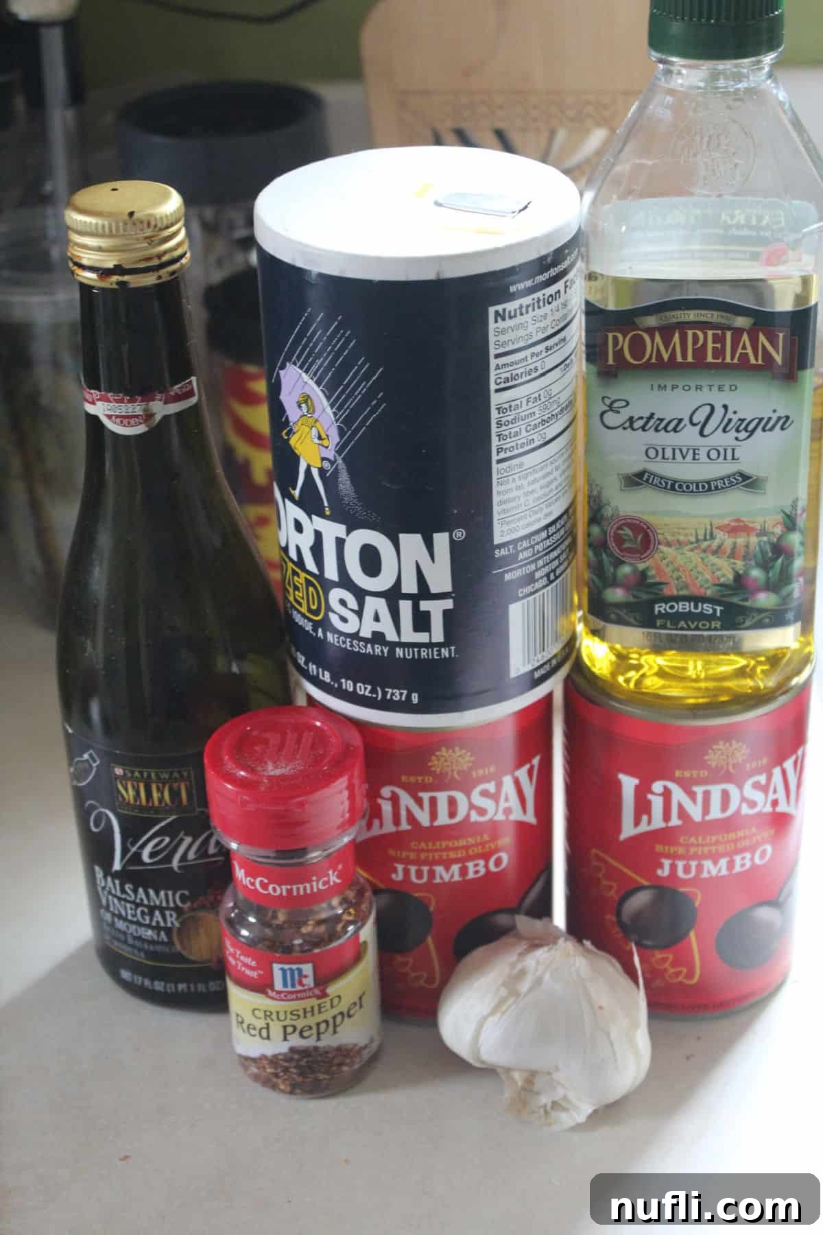 balsamic vinegar, crushed red pepper, salt, two cans of olives, olive oil, and garlic on a white counter