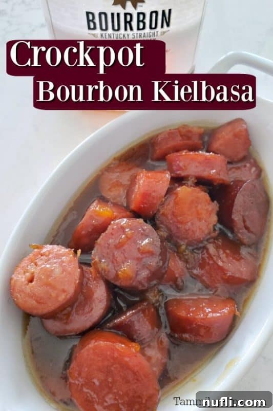 Crockpot Bourbon Glazed Kielbasa served in a white bowl, with a bottle of bourbon in the background.